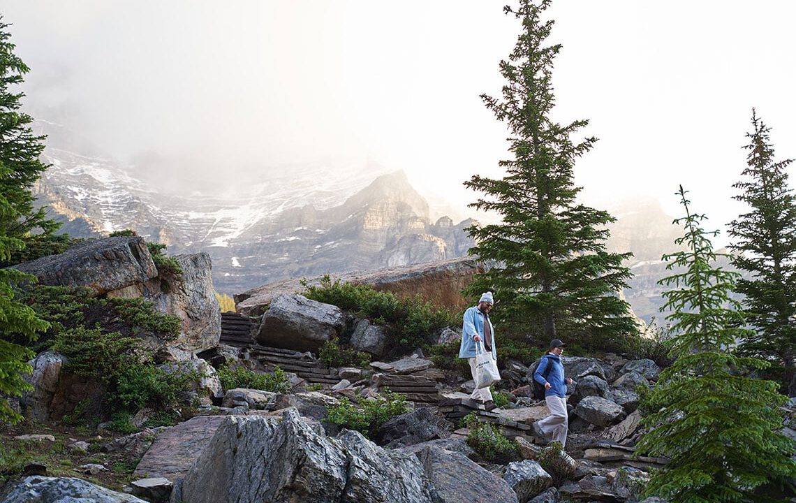 Two people walking down large rock steps in the foreground, mountains in the background