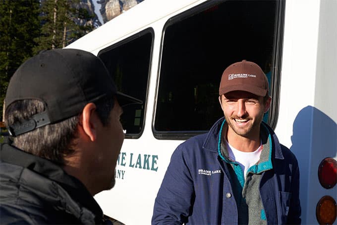 A photo of two men standing by a bus talking. They are both smiling.