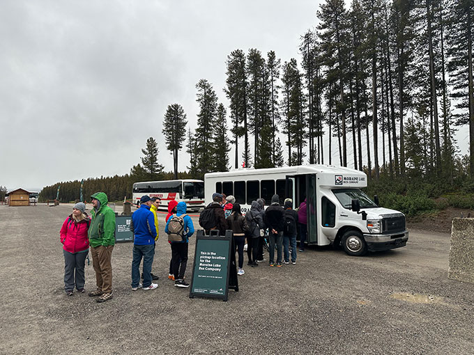 A photo of a white Moraine Lake Bus Company shuttle. It has teal signs on either side. There's a small queue of people boarding